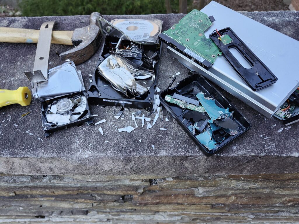 Hammer, pry bar, and broken screwdriver next to pile of destroyed hard drives