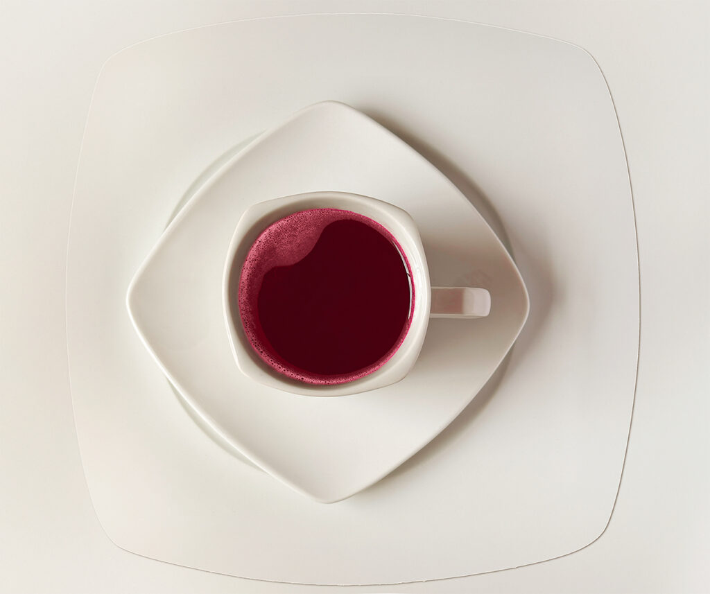 Minimalistic top-view photo of dark red hibiscus tea, in a white cup, on a square white plate, on a white background