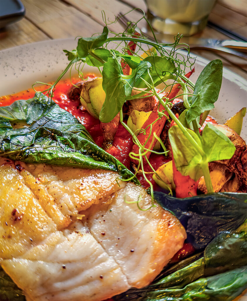White fish in a banana leaf with grilled vegetables over a tomato sauce, topped with microgreens