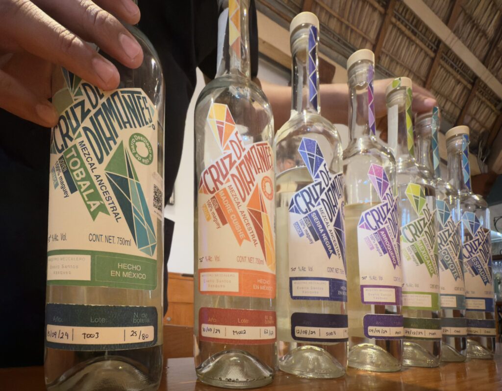A curated flight of seven mezcales, lined up on a wooden board