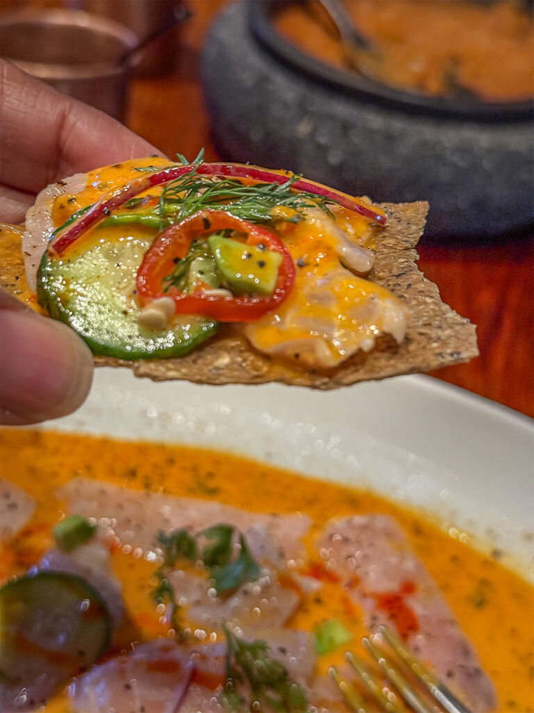 Close-up of a perfect bite of ceviche with vegetables and herbs in bright orange sauce.