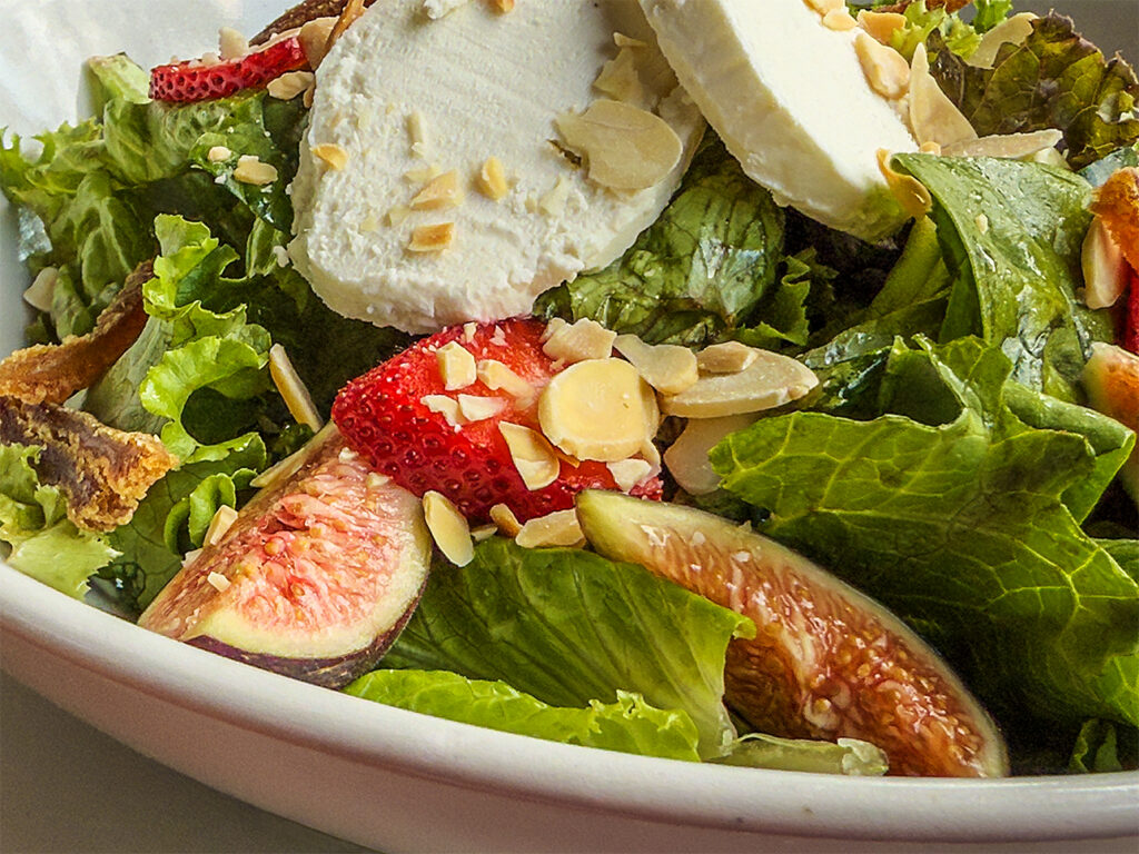 Fresh salad with sliced figs, strawberries, goat cheese rounds, and slivered almonds.
