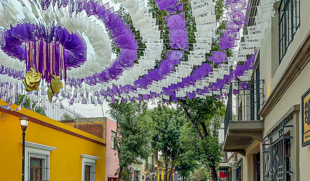 A Oaxacan street with intricately designed, lavender and white flags (papel picado) fluttering overhead