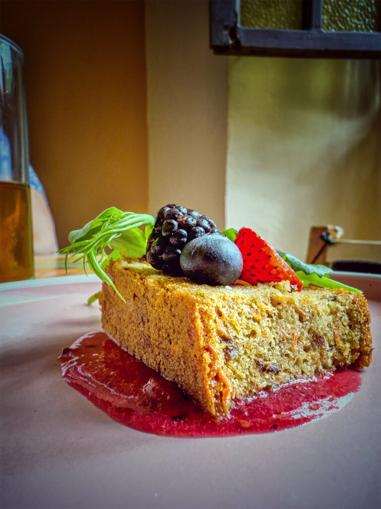 Thick slice of cake in a puddle of berry sauce, topped with fresh berries