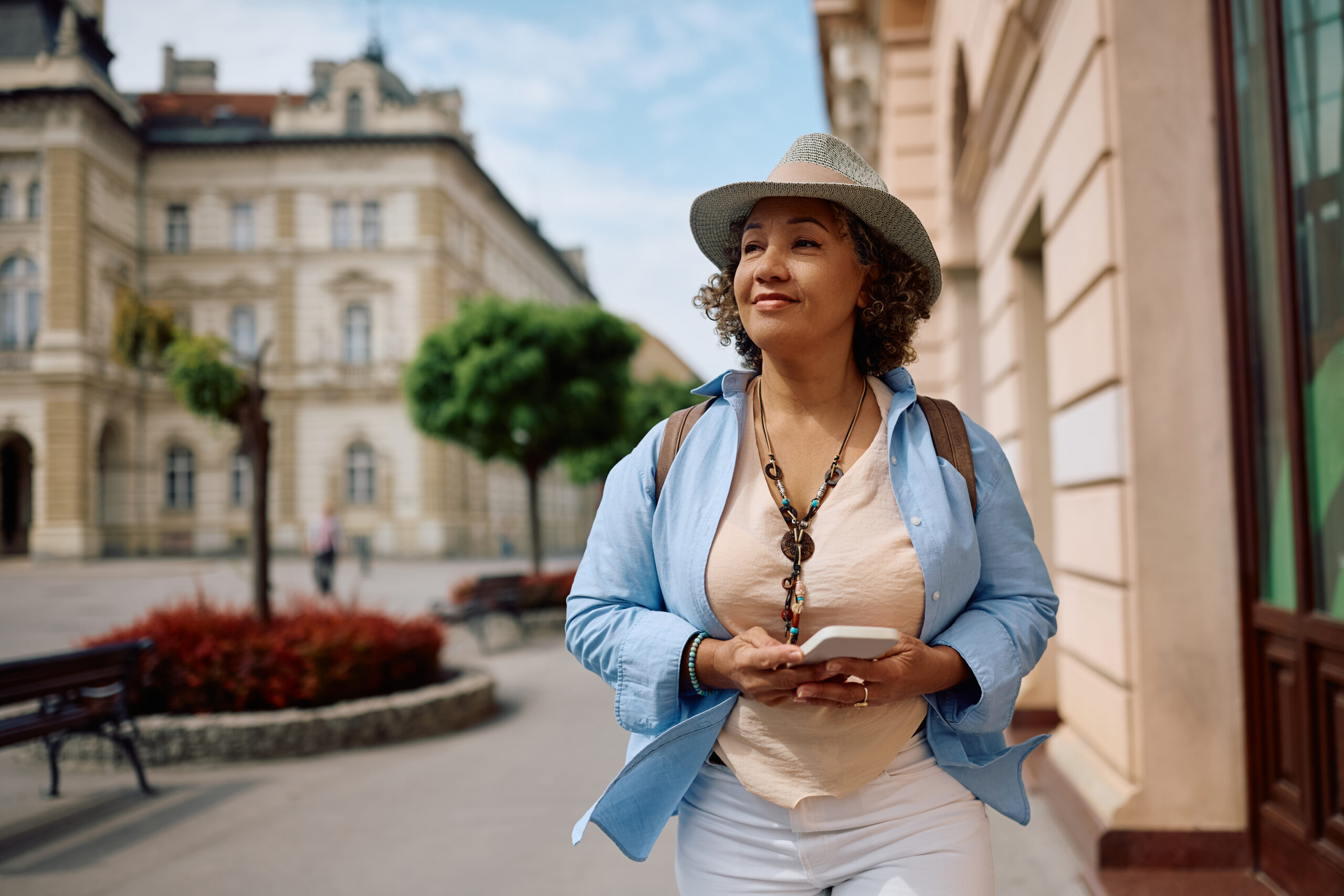 Smiling mature tourist using her cell phone while walking on the street.