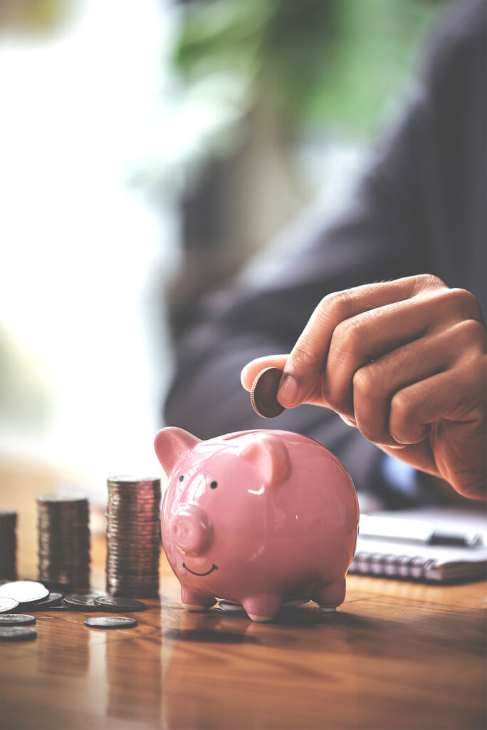 businessman holding a coin over a piggybank on a table